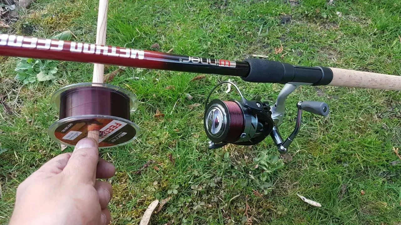 Wędka Method Feeder i kołowrotek z ciemną żyłką. W dłoni szpulka z żyłką, idealna do method feeder.