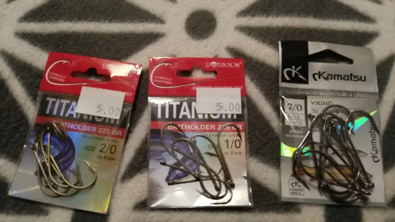 Trzy opakowania haczyków wędkarskich. Dwa z napisem "TITANIUM" i jeden z logo "Kamatsu". Idealny haczyk na lina czeka!