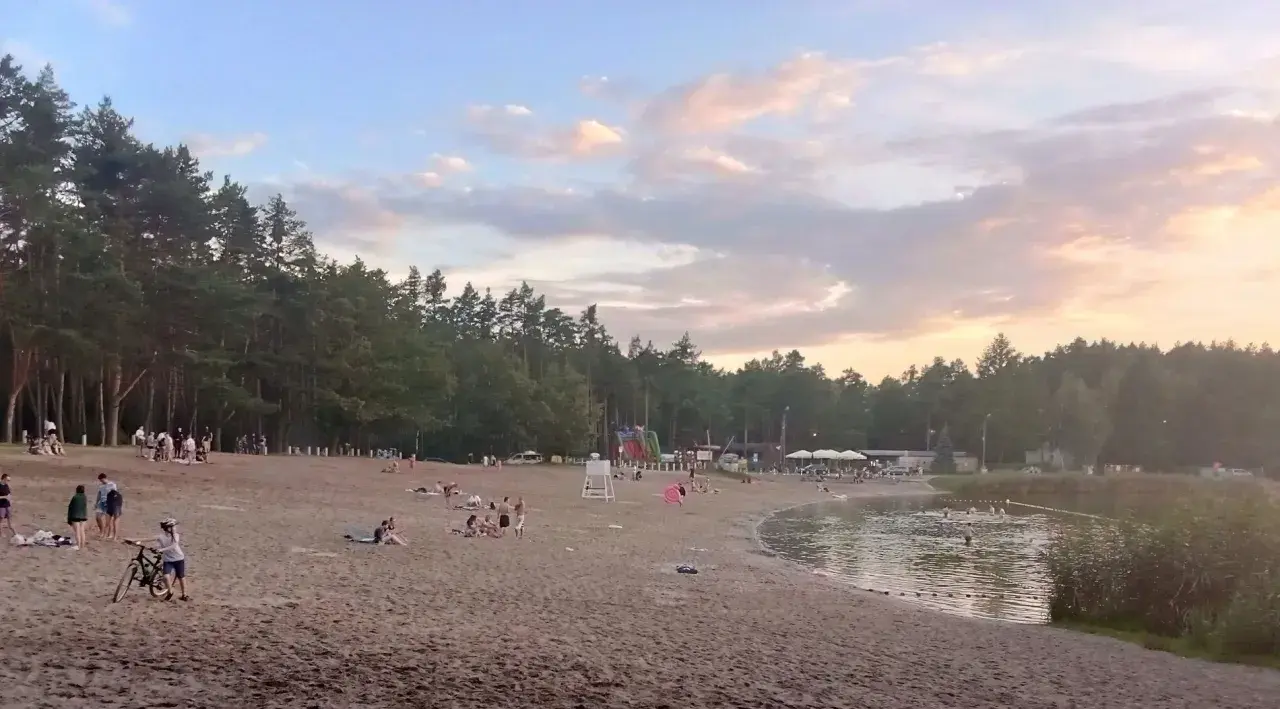 Plaża nad jeziorem w Jelczu Laskowicach, ludzie odpoczywają, dzieci bawią się na dmuchanym zjeżdżalni, a niektórzy kąpią się w wodzie.