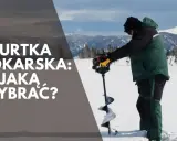 Wędkarz w zielonej kurtce na ryby wierci lód. W tle góry i las.