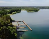 Drewniane pomosty na spokojnym jeziorze Wiartel, otoczonym gęstym lasem. Woda jest przejrzysta, a na pomostach stoją łódki i kajaki.