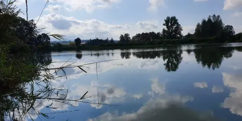 Spokojne jezioro w Czechowicach-Dziedzicach odbija błękitne niebo z chmurami.