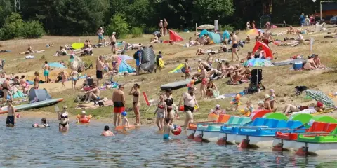 Tłumy ludzi wypoczywają na plaży nad jeziorem Chechło. Woda jest pełna kąpiących się, a na brzegu opalają się plażowicze.