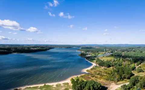 Malownicze jezioro Chańcza otoczone lasami, z piaszczystą plażą i zabudowaniami w tle.