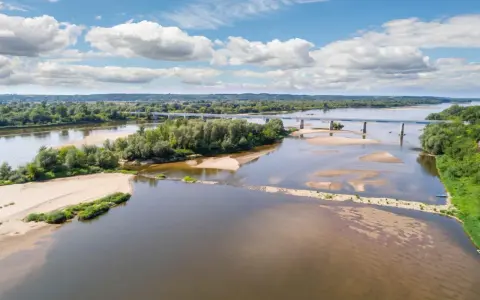 Szeroka Wisła z piaszczystymi łachami i zielonymi wyspami. W oddali most. Woda miejscami płytka, ale gdzieś kryje się wisła głębokość maksymalna.