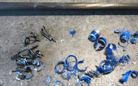 Metalowe przelotki do wędki leżą na szarym blacie, obok niebieskich wiórów i kawałków plastiku.