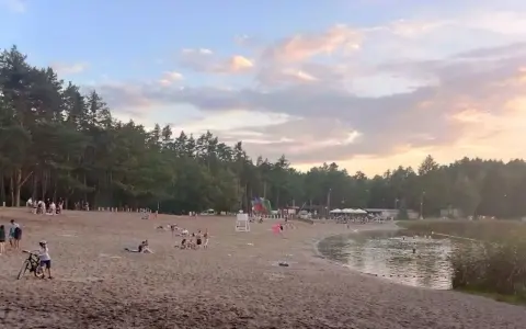 Plaża nad jeziorem w Jelczu Laskowicach, ludzie odpoczywają, dzieci bawią się na dmuchanym zjeżdżalni, a niektórzy kąpią się w wodzie.