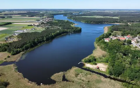 Malownicze jezioro wojnowskie otoczone lasami i polami. W oddali widać zabudowania wsi.