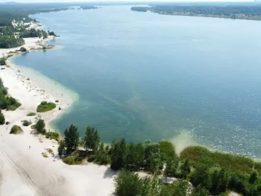 Plaża nad jeziorem, piasek, drzewa i ludzie odpoczywający w słońcu. Idealne miejsce na wakacje, jak z **pogoria** 1.