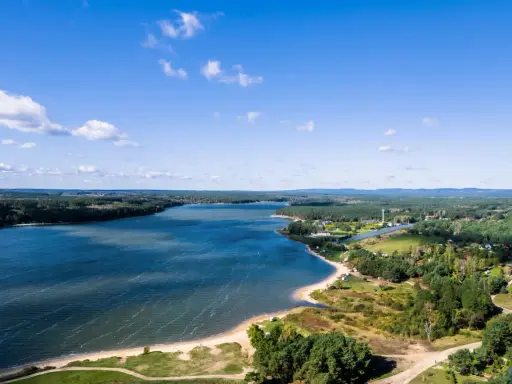 Malownicze jezioro Chańcza otoczone lasami, z piaszczystą plażą i zabudowaniami w tle.