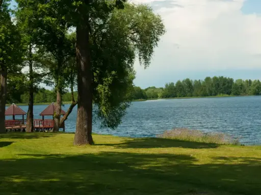 Malownicze jezioro Grabowo z altanami na pomoście, otoczone zielenią i drzewami.