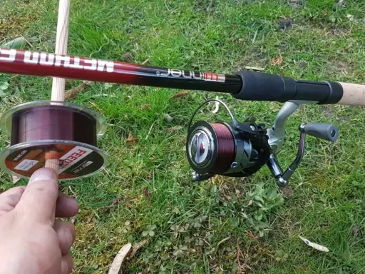 Wędka Method Feeder i kołowrotek z ciemną żyłką. W dłoni szpulka z żyłką, idealna do method feeder.