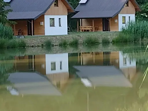 Urokliwe łowisko z domkami letniskowymi, których odbicia tańczą na spokojnej tafli wody.