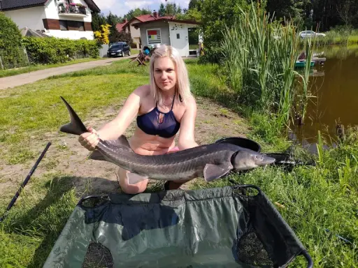 Kobieta z okazałym jesiotrem na łowisku pod lasem.