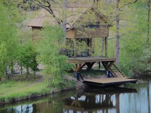 Drewniane domki wędkarskie nad jeziorem, otoczone zielenią, z pomostami schodzącymi do wody.