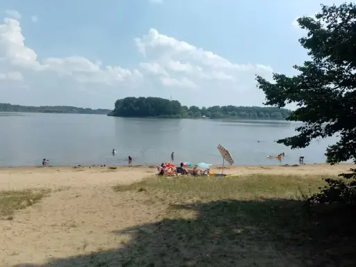 Słoneczny dzień nad jeziorem przeczyckim. Ludzie odpoczywają na piaszczystej plaży, kąpią się i pływają.