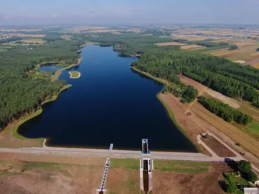 Widok z lotu ptaka na zalew Jagodno otoczony lasem i polami. Na pierwszym planie zapora z budowlami technicznymi.
