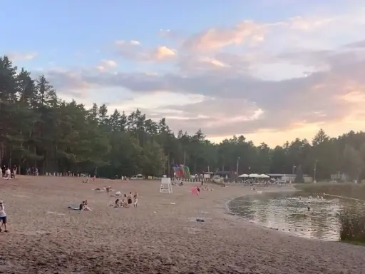 Plaża nad jeziorem w Jelczu Laskowicach, ludzie odpoczywają, dzieci bawią się na dmuchanym zjeżdżalni, a niektórzy kąpią się w wodzie.