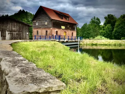 Stara ceglana budowla nad jeziorem Cekcyn, z drewnianą przybudówką i pomostem.