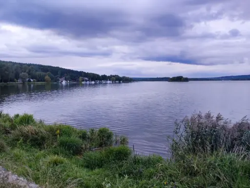 Spokojny zalew wióry, z łodziami przy brzegu i lasem w tle, pod burzliwym niebem.