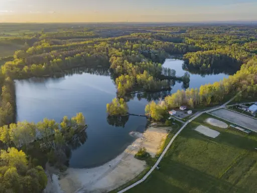Malownicze jezioro Czechowice otoczone zielonym lasem, z piaszczystą plażą i zabudowaniami rekreacyjnymi.