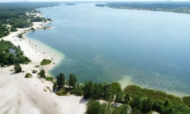 Plaża nad jeziorem, piasek, drzewa i ludzie odpoczywający w słońcu. Idealne miejsce na wakacje, jak z **pogoria** 1.