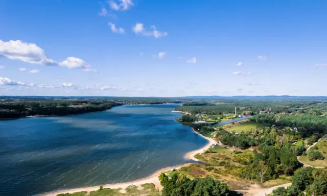 Malownicze jezioro Chańcza otoczone lasami, z piaszczystą plażą i zabudowaniami w tle.