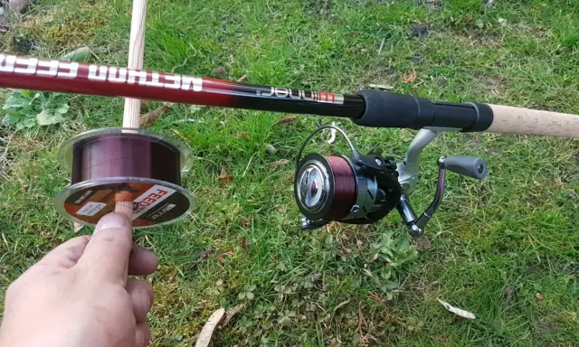 Wędka Method Feeder i kołowrotek z ciemną żyłką. W dłoni szpulka z żyłką, idealna do method feeder.