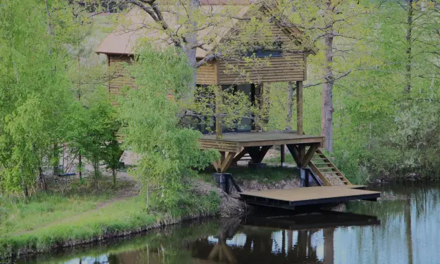 Drewniane domki wędkarskie nad jeziorem, otoczone zielenią, z pomostami schodzącymi do wody.