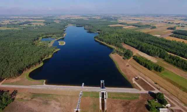 Widok z lotu ptaka na zalew Jagodno otoczony lasem i polami. Na pierwszym planie zapora z budowlami technicznymi.