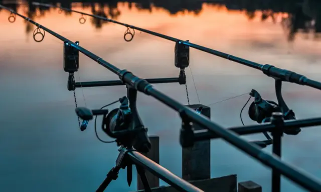 Dwa wędki feederowe ustawione nad wodą o zachodzie słońca. Podpórka feeder stabilnie trzyma sprzęt, gotowy na branie.