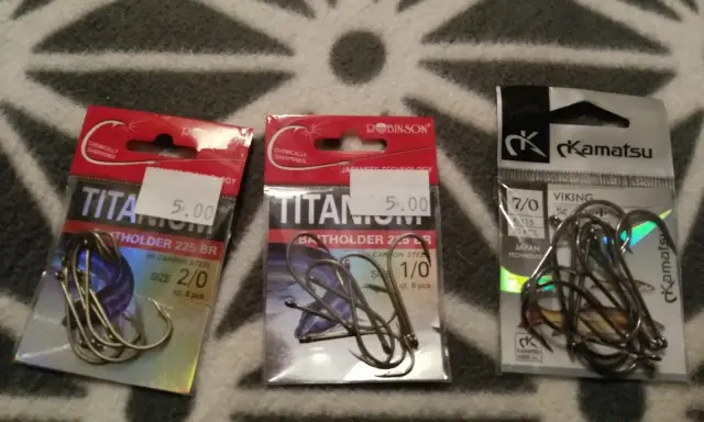 Trzy opakowania haczyków wędkarskich. Dwa z napisem "TITANIUM" i jeden z logo "Kamatsu". Idealny haczyk na lina czeka!