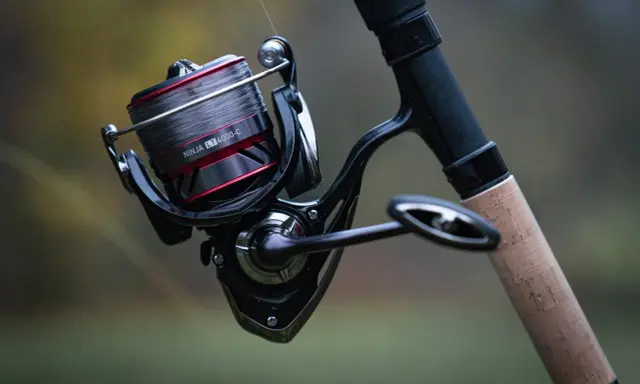 Czarne, nowoczesne detale budowy kołowrotka wędkarskiego Daiwa Ninja LT 4000-C z szarą żyłką i korkową rękojeścią.