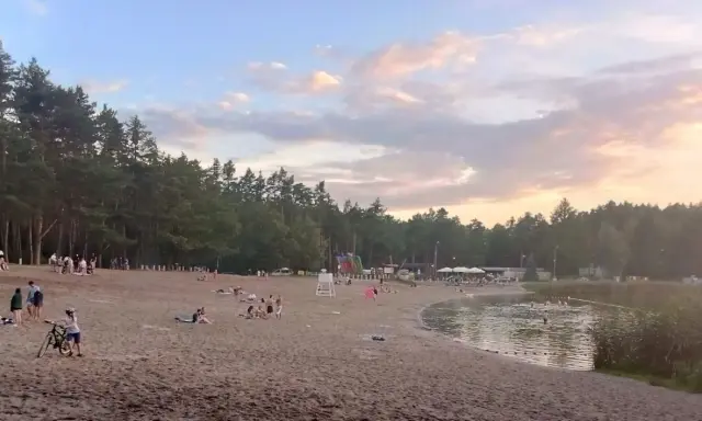 Plaża nad jeziorem w Jelczu Laskowicach, ludzie odpoczywają, dzieci bawią się na dmuchanym zjeżdżalni, a niektórzy kąpią się w wodzie.