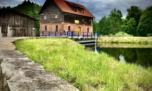 Stara ceglana budowla nad jeziorem Cekcyn, z drewnianą przybudówką i pomostem.