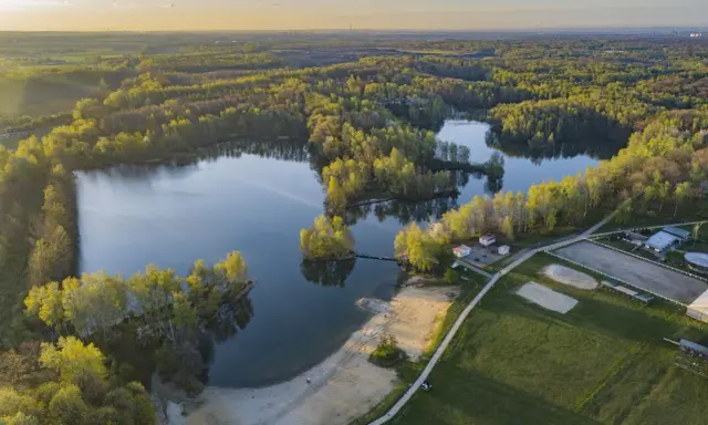 Malownicze jezioro Czechowice otoczone zielonym lasem, z piaszczystą plażą i zabudowaniami rekreacyjnymi.