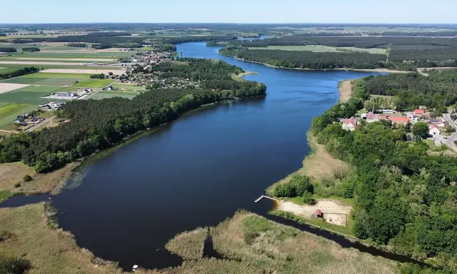 Malownicze jezioro wojnowskie otoczone lasami i polami. W oddali widać zabudowania wsi.