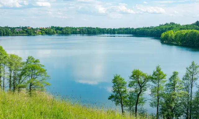 Malownicze żnin jezioro otoczone zielenią, z widocznymi domami na horyzoncie i błękitnym niebem z chmurami.