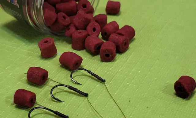 Czerwone kulki zanętowe i haczyki wędkarskie. Różne rozmiary haczyków wędkarskich i kulek.