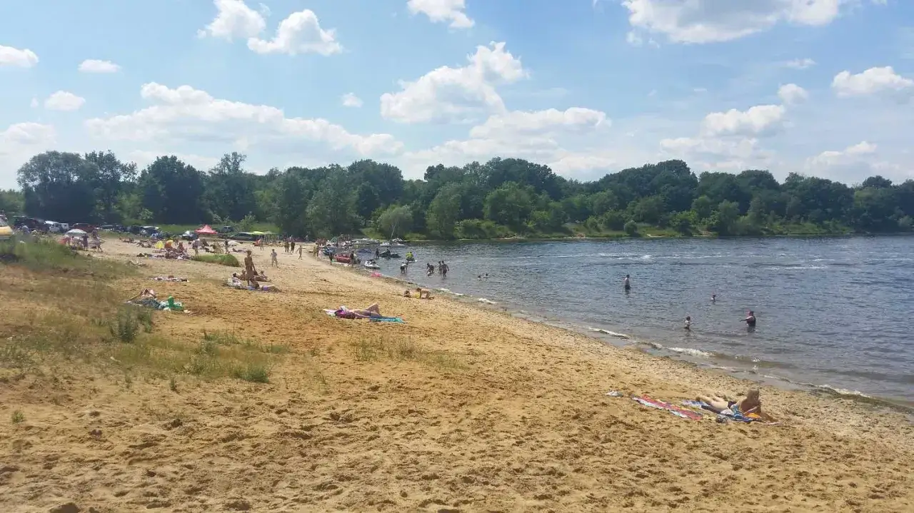 Słoneczny dzień nad rzeczyce jezioro. Ludzie odpoczywają na piaszczystej plaży, kąpią się i pływają.