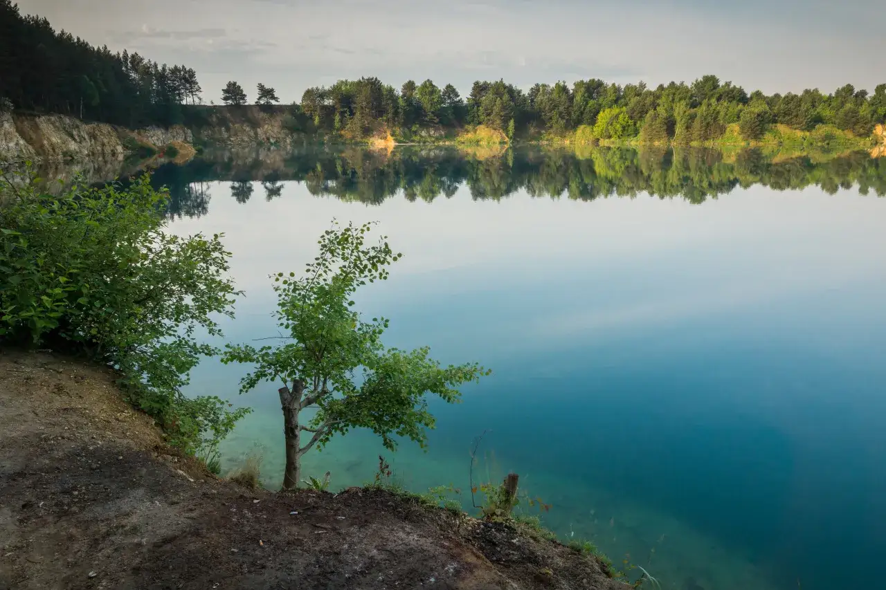 Spokojne jezioro wapienne z odbijającymi się w wodzie drzewami i piaszczystym brzegiem.