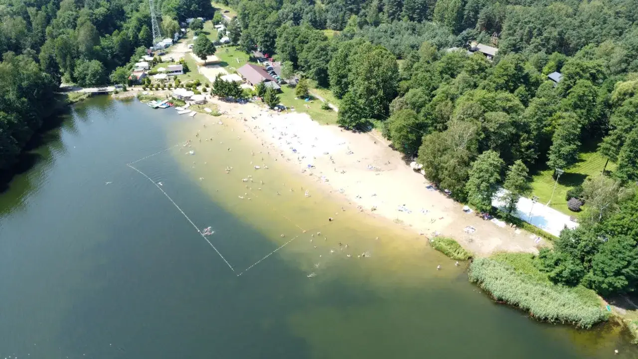 Słoneczny dzień nad zalewem Rogoźnik. Ludzie odpoczywają na piaszczystej plaży i kąpią się w jeziorze.