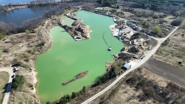 Widok z lotu ptaka na turkusowe jezioro zajączkowskie, otoczone piaszczystymi skarpami i zielenią. Widać sprzęt wydobywczy i łódź.